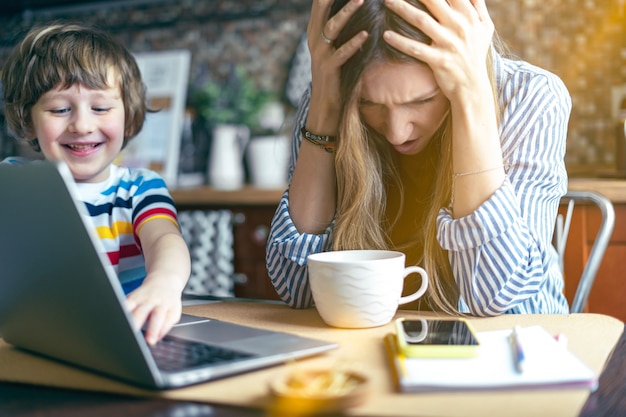 Madre que trabaja desde casa en línea con el niño. Estresado con laptop