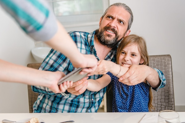 Madre quitando tableta digital de hija y padre