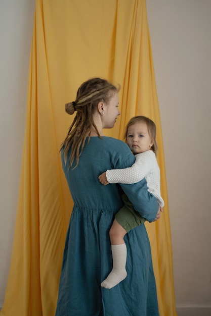 Una madre con rastas con un bebé en brazos sobre un fondo amarillo de tela Primer plano