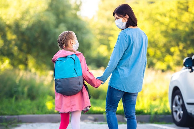 Madre reuniendo a una alumna de primaria después de las clases sobre el aparcamiento al aire libre durante la epidemia del virus