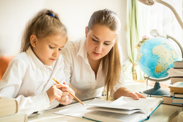 Madre sentada con su hija en el escritorio y explicando la complicada tarea en la tarea