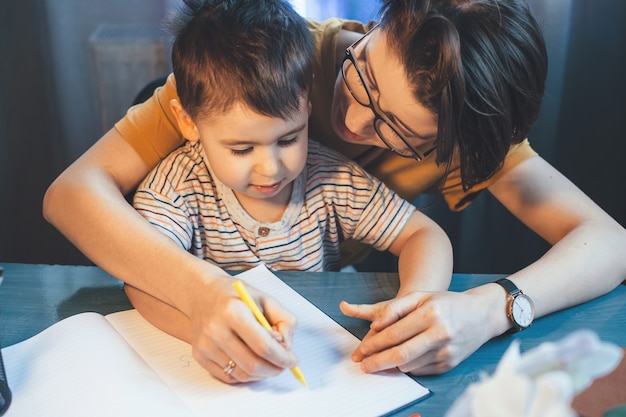 Madre servicial caucásica está enseñando a su hijo a escribir sosteniendo su mano