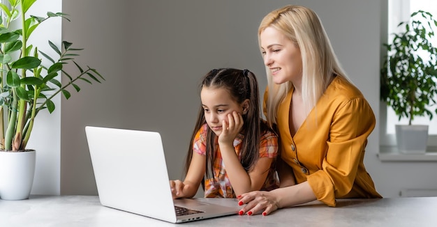 Madre servicial explicándole a su hija cómo usar una computadora portátil.