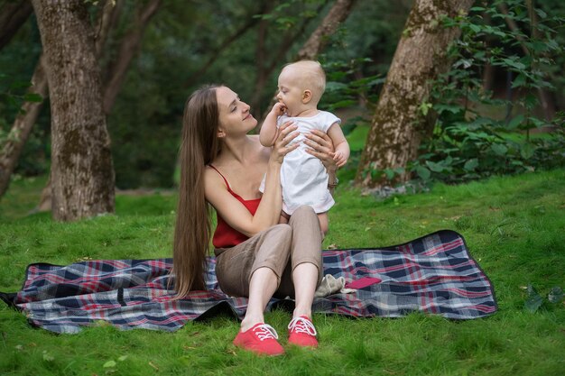 La madre se sienta en una manta y sostiene a un bebé Picnic con un niño pequeño