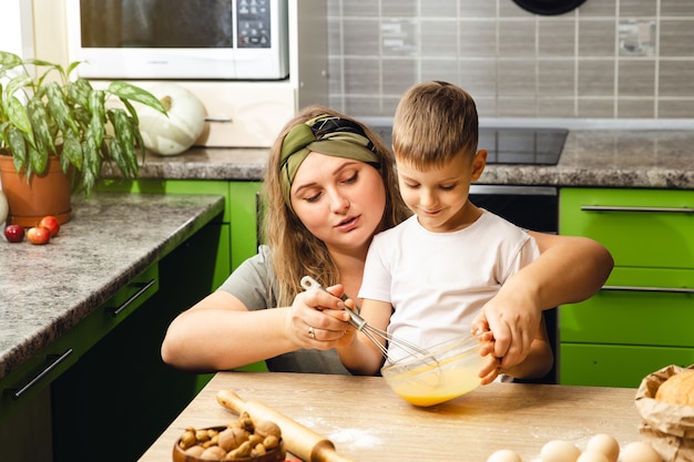 Madre solícita ayuda al pequeño hijo en edad preescolar a preparar galletas, madre amorosa sonriente a aprender a cocinar con un niño pequeño, preparando el almuerzo el fin de semana en la cocina juntos