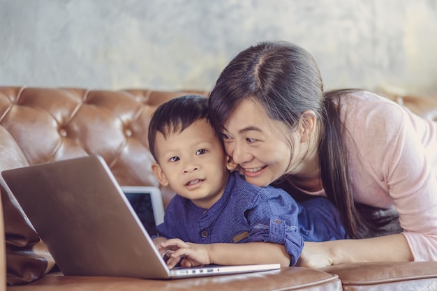 Una madre soltera asiática con su hijo está mirando la caricatura a través del portátil de tecnología y jugando juntos