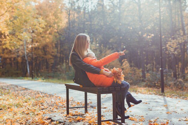 La madre soltera y el niño niño en el otoño en el parque se sientan en la temporada de otoño del banco y el concepto de familia