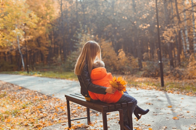 La madre soltera y el niño niño en el otoño en el parque se sientan en la temporada de otoño del banco y el concepto de familia