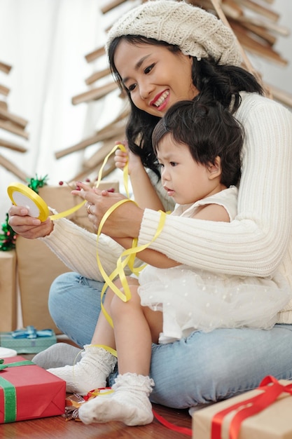 Madre sonriente abrazando a su hija desenrollando la cinta amarilla para la decoración navideña