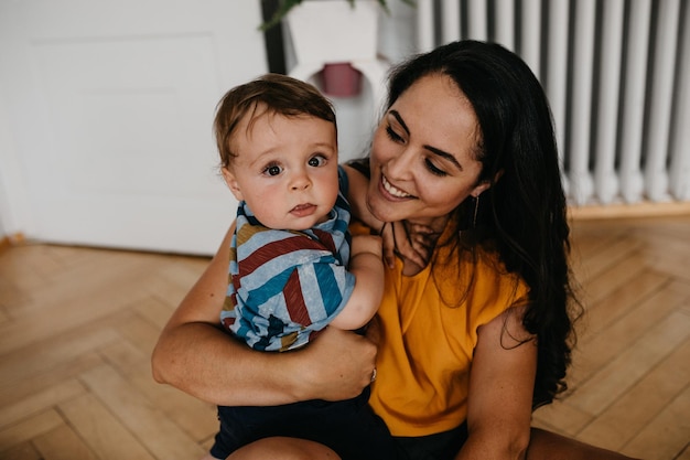 Foto madre sonriente con el bebé sentado en el suelo de madera