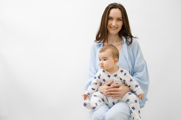 Madre sonriente con el bebé en su regazo sentado sobre fondo blanco retrato de mujer en ropa azul concepto del día de la madre cuidando a un niño pequeño