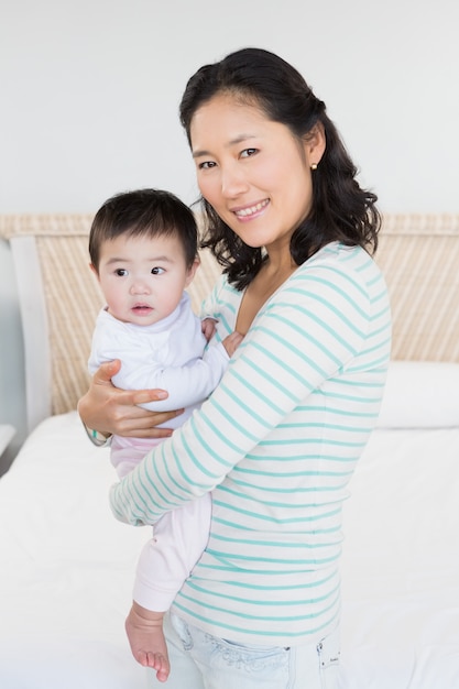 Madre sonriente que lleva a la hija del bebé en dormitorio