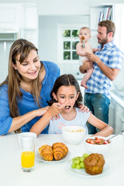 Madre sonriente que mira a la hija que desayuna en cocina