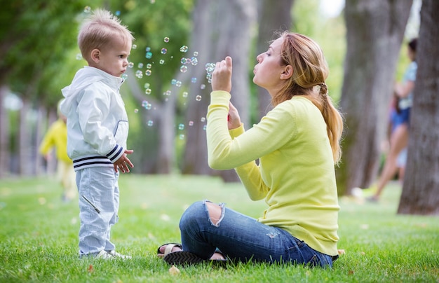 Madre soplando pompas de jabón al aire libre y su pequeño hijo mirándola