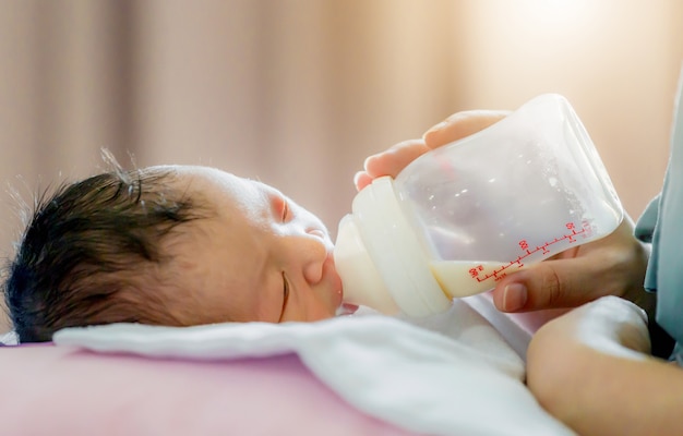 Madre sosteniendo y alimentando al bebé recién nacido de la botella de leche, concepto de amor