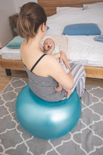 Madre sosteniendo y balanceando al bebé sentado en fitball