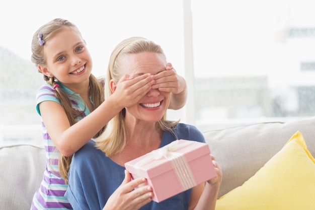 Madre sosteniendo regalo con hija cubriendo sus ojos