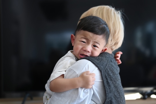 Madre sosteniendo a su hijo llorando sala de estar en casa.