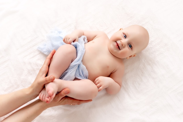 Una madre sostiene suavemente las piernas de su bebé, un niño sonriente yace de espaldas en una cama blanca.