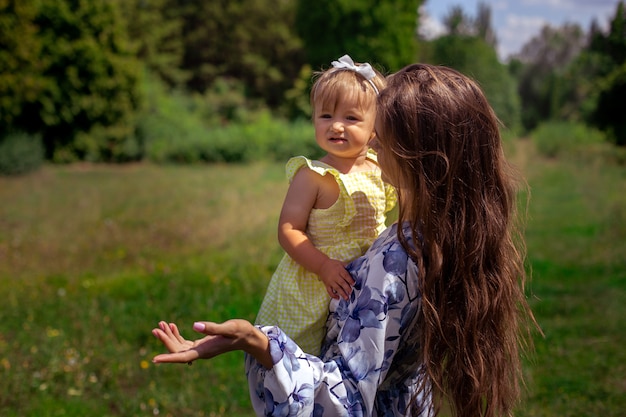 Madre con su hermosa hijita en sus manos habla y señala a un lado en el parque verde