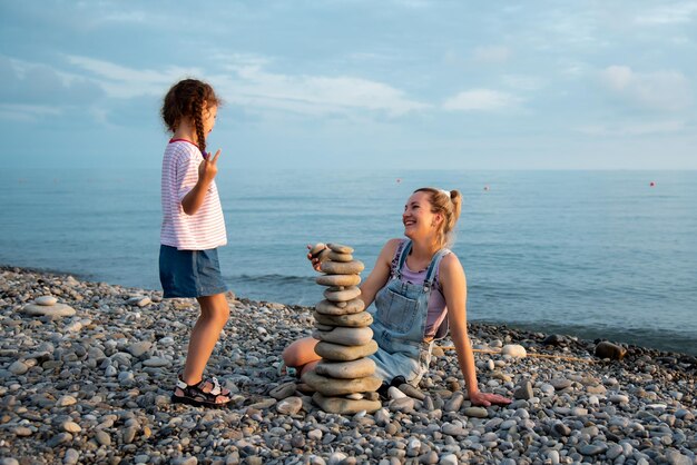 Una madre y su hija de 6 años en la playa construyen un castillo de piedras Vacaciones familiares de verano