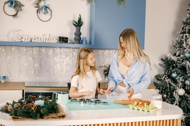 La madre y su hija cocinan galletas de jengibre navideñas en la cocina