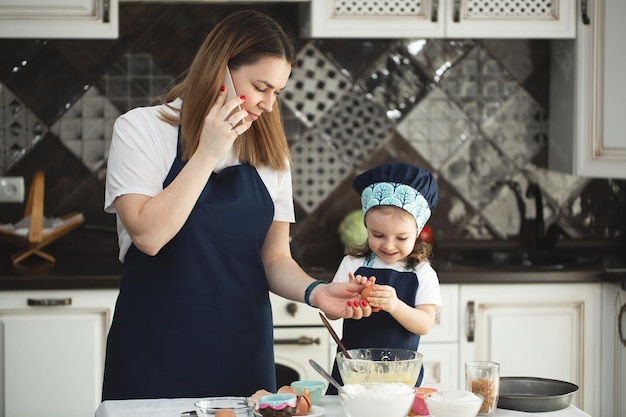 Una madre y su hija con delantales idénticos y gorros de chef están cocinando en la cocina.