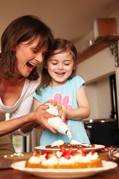 Una madre y su hija glaseando un pastel juntas en casa