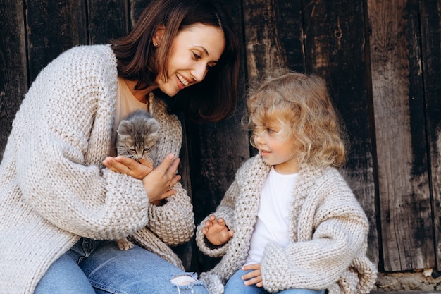 Madre y su hija juegan con un gatito junto a la pared de madera.