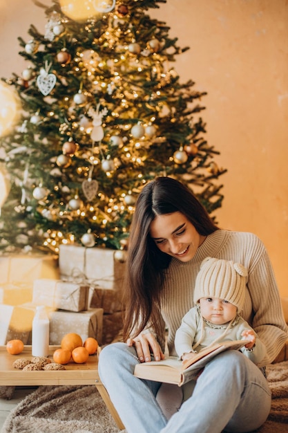 Madre con su hija leyendo un libro junto al árbol de Navidad