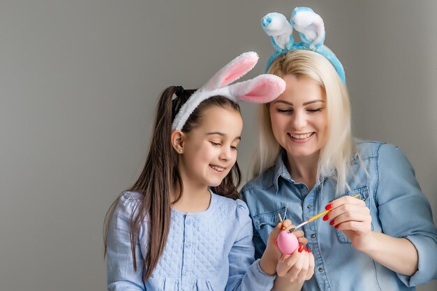 Madre y su hija pintando huevos. Familia feliz preparándose para Pascua. Niña pequeña y linda con orejas de conejo.