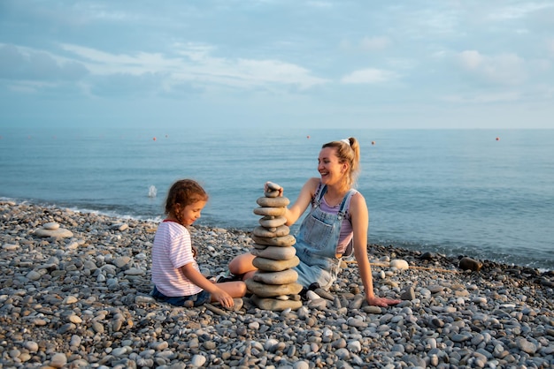 Una madre y su hija en la playa construyen un castillo de piedras Vacaciones familiares de verano