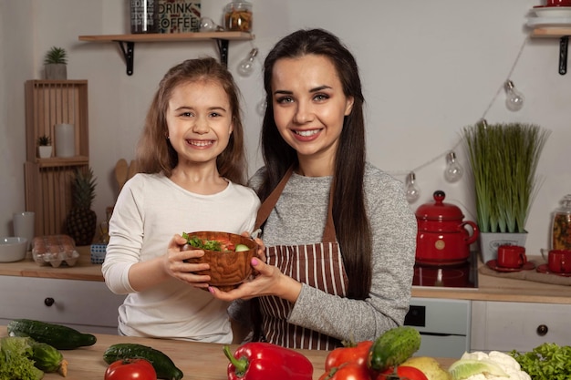 La madre y su hija preparan una ensalada de verduras y se divierten en la cocina.