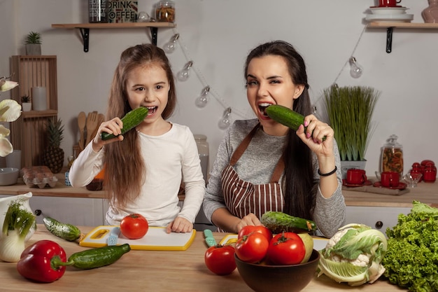 La madre y su hija preparan una ensalada de verduras y se divierten en la cocina.