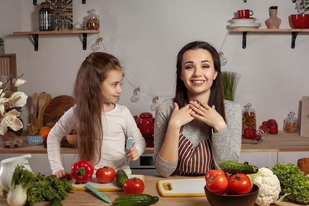 La madre y su hija preparan una ensalada de verduras y se divierten en la cocina.