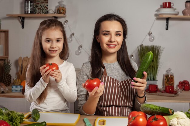 La madre y su hija preparan una ensalada de verduras y se divierten en la cocina.