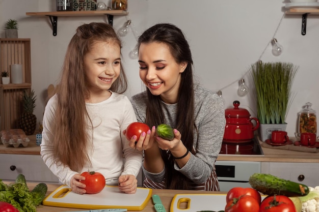 La madre y su hija preparan una ensalada de verduras y se divierten en la cocina.