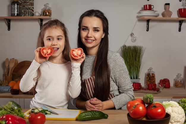 La madre y su hija preparan una ensalada de verduras y se divierten en la cocina.