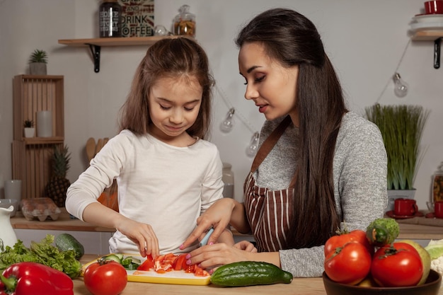 La madre y su hija preparan una ensalada de verduras y se divierten en la cocina.
