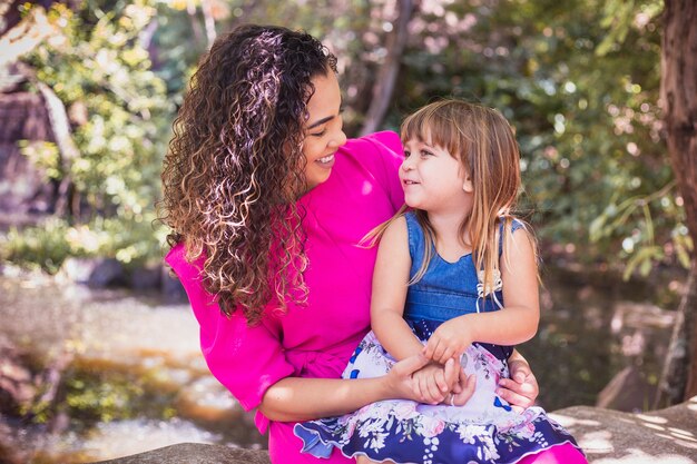 Madre con su hija en su regazo en el parque. Hermosa joven madre con su hija en el parque. Día de la Madre