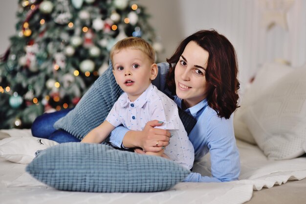 Madre con su hijo acostado en la cama en el fondo de un árbol de Navidad
