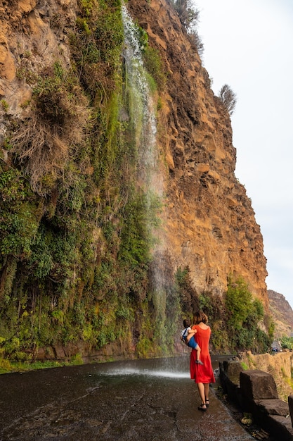 Una madre con su hijo en la cascada que cae en la carretera llamada Cascada Anjos Madeira Portugal