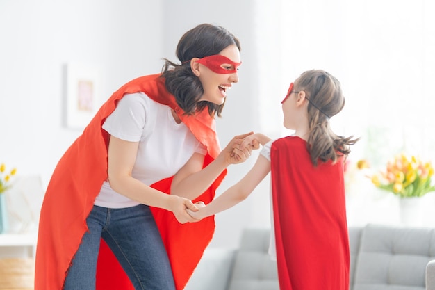 Madre y su hijo jugando juntos Chica y mamá en traje de superhéroe