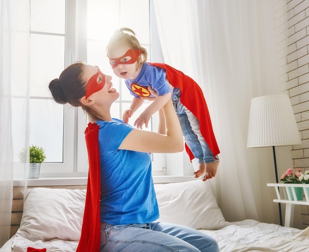 Madre y su hijo jugando juntos Chica y mamá en traje de superhéroe