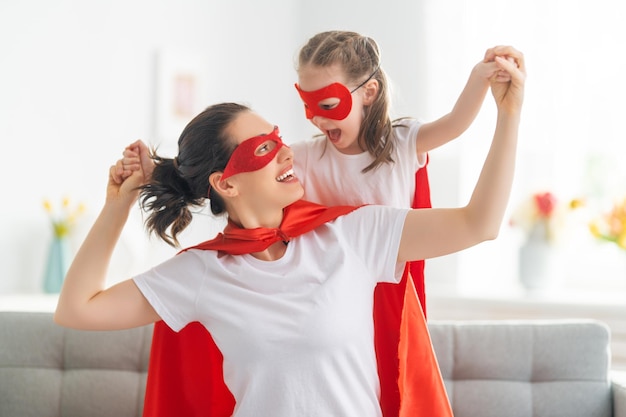 Foto madre y su hijo jugando juntos chica y mamá en traje de superhéroe