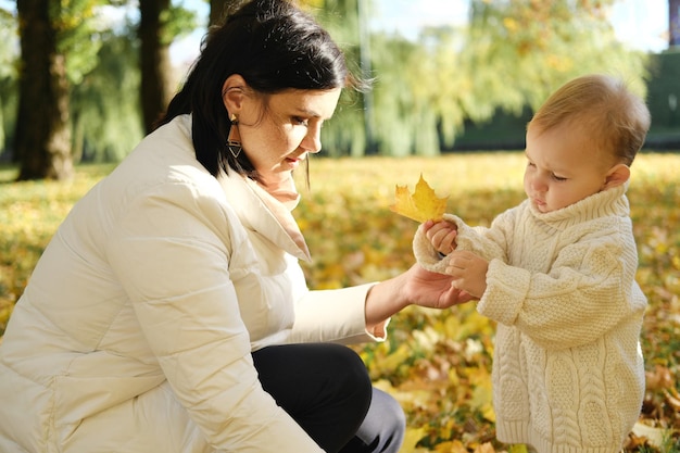 Madre con su hijo pequeño camina en el parque de otoño La madre le da a su hijo una hoja amarilla de otoño