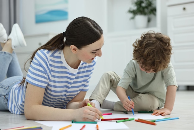 Madre y su hijo pequeño dibujando con marcadores de colores en el suelo de casa