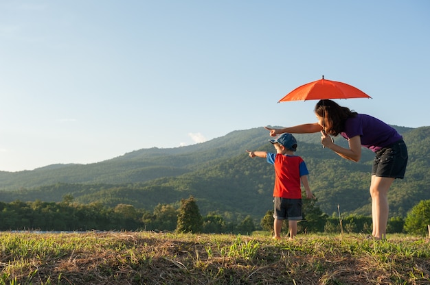 Una madre y su hijo sosteniendo paraguas al aire libre al atardecer