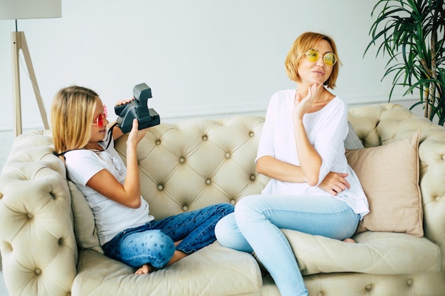 La madre y su pequeña hija se abrazan, posan y hacen una foto selfie en un teléfono inteligente mientras se sientan en el sofá de casa