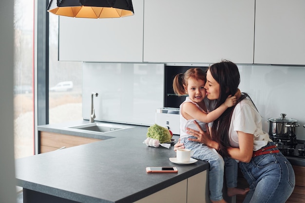 Madre con su pequeña hija abrazándose en el interior de la cocina